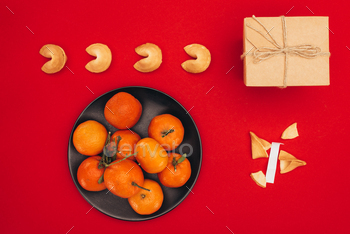 top view of chinese fortune cookies and tangerines on red surface as chinese new year composition