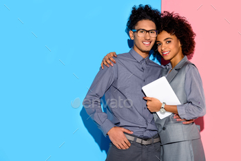 Young african amercian businesswoman holding tablet and hugging stylish businessman on pink and blue