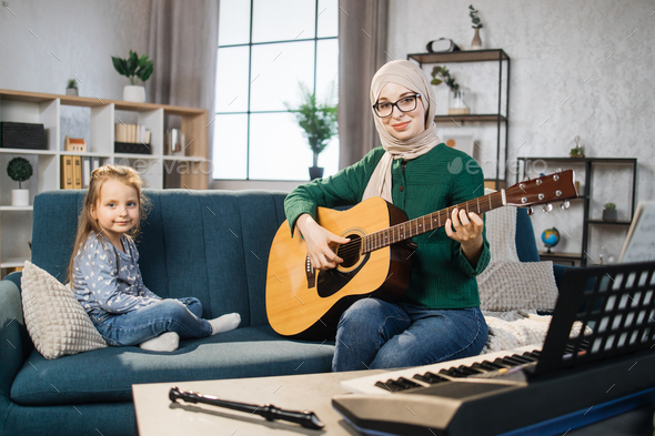 Little cute girl with music muslim teacher having lesson at guitar at school of music.