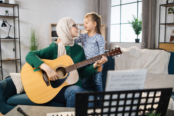 Muslim mom and little happy girl in music therapy by playing guitar on music room.