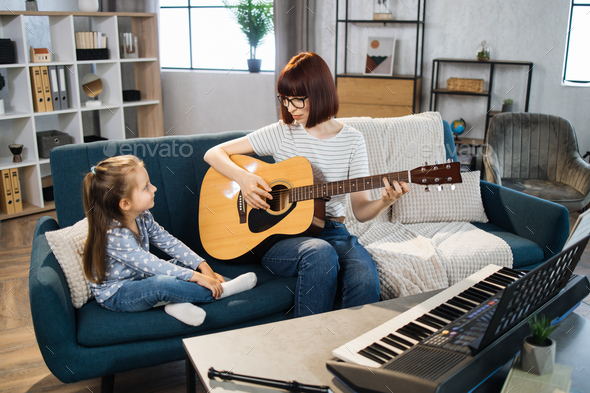 Mom and little happy girl in music therapy by playing guitar on music room.