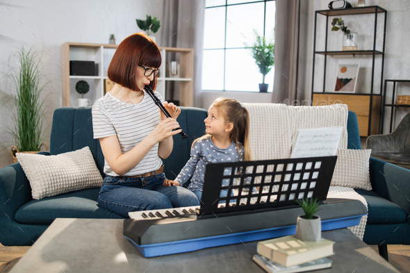 Mom and little happy girl in music therapy by playing flute on music room.