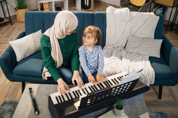 Muslim mom and little happy girl in music therapy by playing piano on music room.