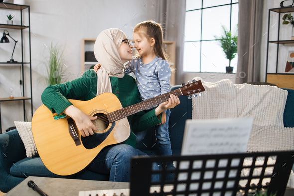 Muslim mom and little happy girl in music therapy by playing guitar on music room.