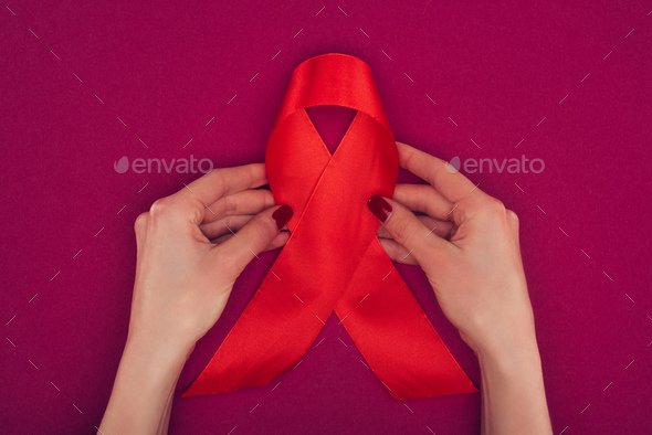cropped view of hands with big red aids ribbon, isolated on pink