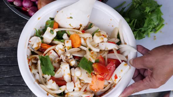 Mixing squid and vegetable dish with spoon for serving, top down shot alt