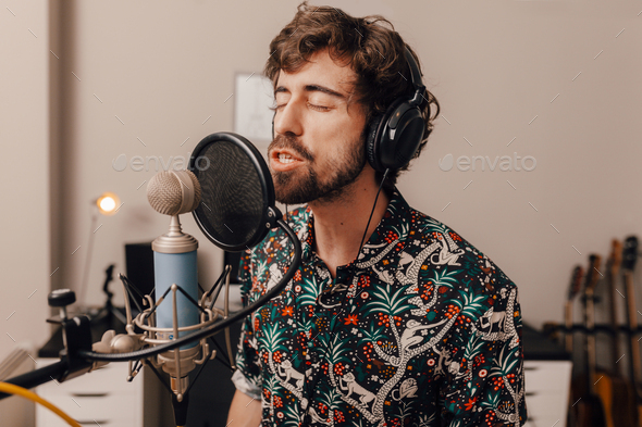 Millenial male singer on headphones singing at recording home studio
