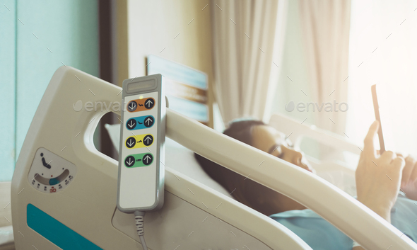 Hospital bed remote control hanging on the bed rail with woman patient on bed in hospital room.