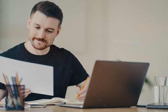 Skilled professional male expert busy doing paper report edits online files via laptop