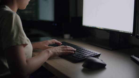 Young female typing text working on computer at night from a home office.