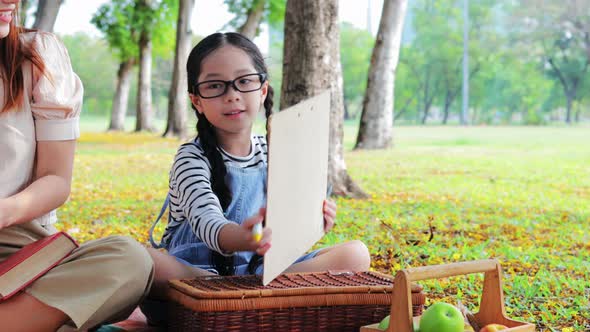 Happy Asian Daughter, son, and mon drawing a picture together during picnic in park