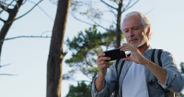 Senior man clicking photos with mobile phone at countryside alt