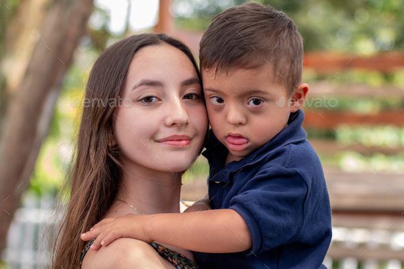 Portrait of a girl holding her brother with Down syndrome. Disability, inclusion and diversity.