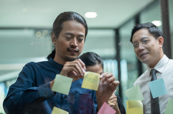 Asian business team meeting in the office using post it notes stick on glass wall