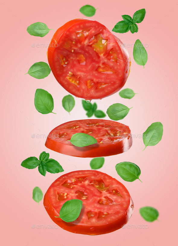 Round red slices of tomato and basil leaves levitate on a pink background.