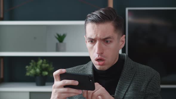 Stressed Businessman is Shocked While Using Smartphone on Modern Office Background