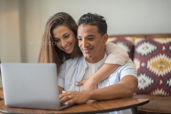 Happy young couple at home using laptop together surfing the web. Concept of new life and love