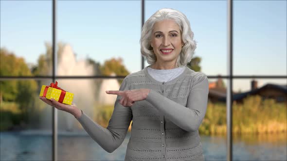 Happy Senior Woman Pointing at Gift Box in Her Palm alt