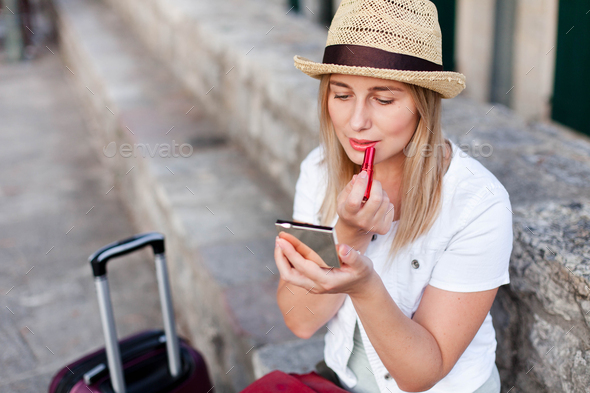 Girl traveler corrects makeup and applies red lipstick