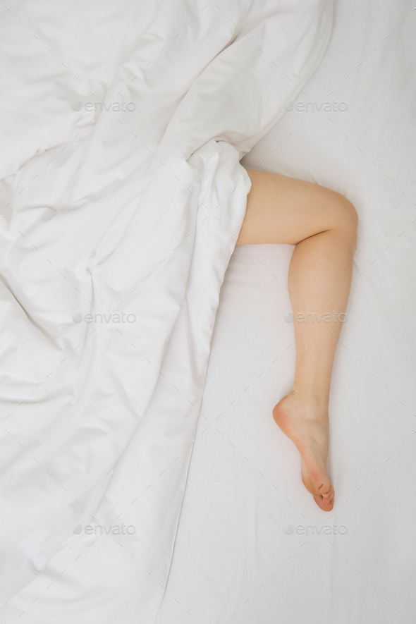 Lifestyle photo of woman under the blanket on the bed, her leg is