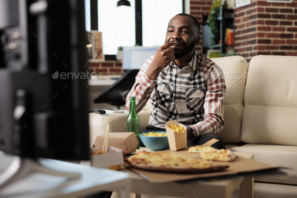 African american man eating chips while he watches film on tv