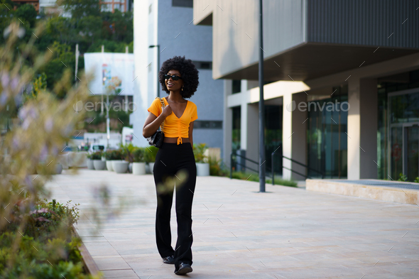 Photo of a stylish young black woman with curly hair wearing orange crop top walking in the street