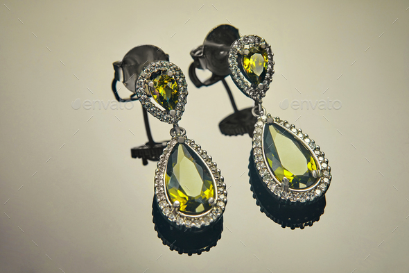 White gold earrings with diamonds and yellow-green stones on a gradient background with reflection