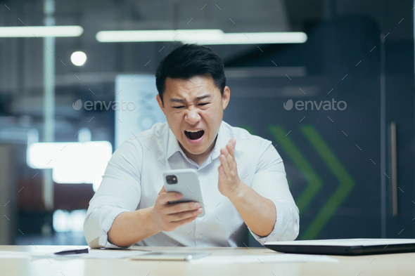 Angry businessman in office yelling on the phone, Asian man frustrated with received email