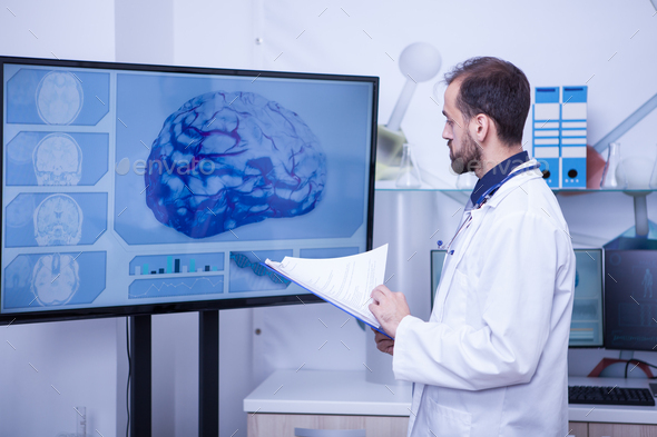 Doctor with clipboard on his hand looking at a brain on a big monitor