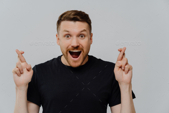 Young happy guy believer with open mouth crossing fingers for best luck