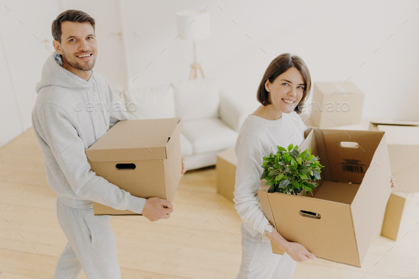 Positive female and male property owners pose with personal belongings in carton