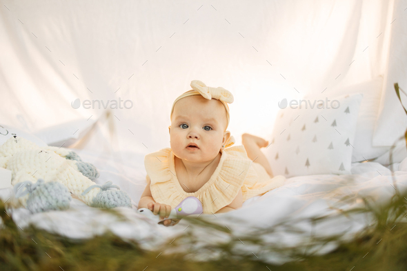 Cute healthy little girl in a yellow dress lyuing on green grass in the park on white blanket