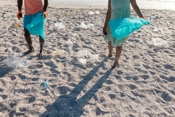 Low section of african american couple picking plastic waste on sand at beach - Stock Photo - Images