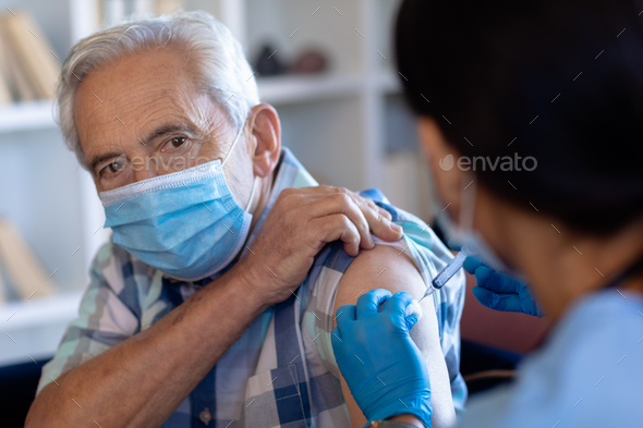 Biracial female health worker giving an injection to caucasian senior man at home - Stock Photo - Images