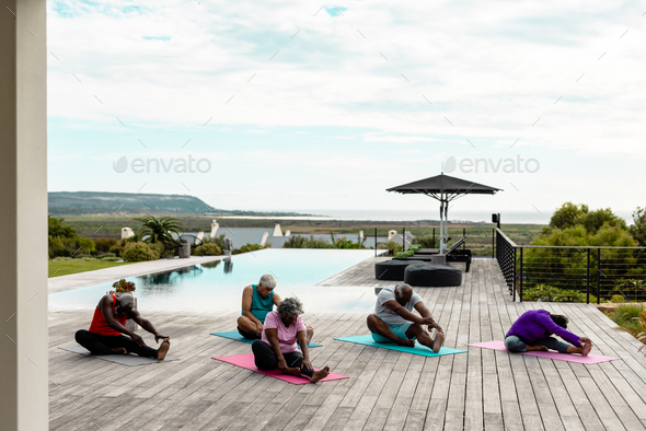 Multiracial senior friends exercising on hardwood floor at poolside against sky in yard - Stock Photo - Images