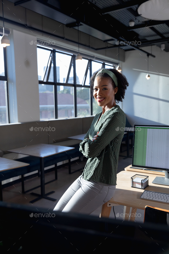 Portrait of smiling african american young businesswoman with arms crossed in office - Stock Photo - Images
