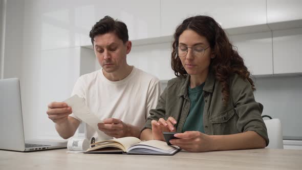 Husband and Wife are Sitting at the Kitchen Table with a Laptop and Calculating Expenses Forming a alt