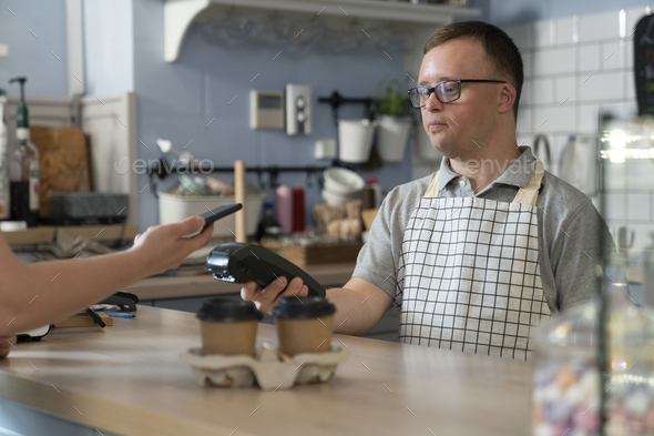 Caucasian man with down syndrome accepting contactless payment in the cafe