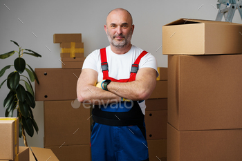 Portrait of a middle-aged man mover in uniform standing against stacked boxes