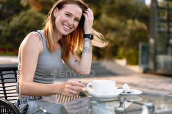 Beautiful cute young woman while drinking tea in modern street cafe