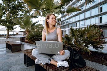 Young beautiful casual woman working on a laptop sitting on the bench in the street