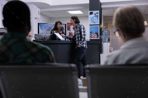 Private clinic receptionist giving assistance to asian patient to complete hospital admission form - Stock Photo - Images