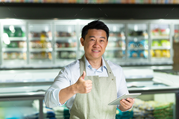 Asian supermarket worker looks into the camera and smiles shows thumbs up