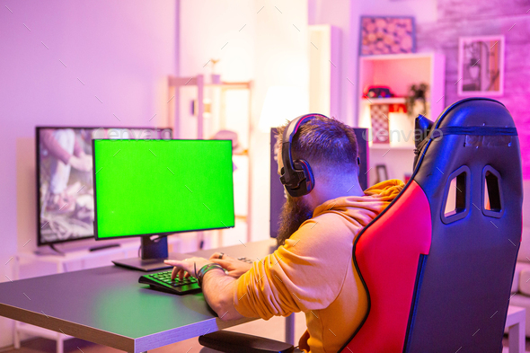 Man playing on powerfull gaming pc in a room with neon lights on a green screen computer