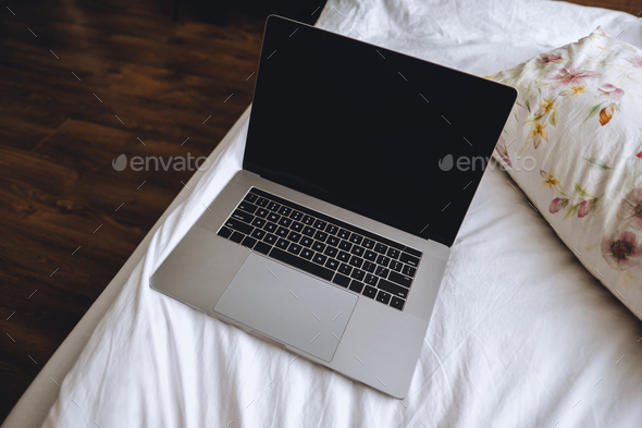 Laptop on a white bed with floral pillows. Work at home, concept of remote work freelancer