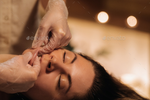 A cosmetologist girl does a facial and neck massage to a girl in the office for skin elasticity