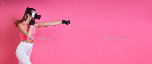 Confident young woman in virtual reality glasses boxing against pink background - Stock Photo - Images