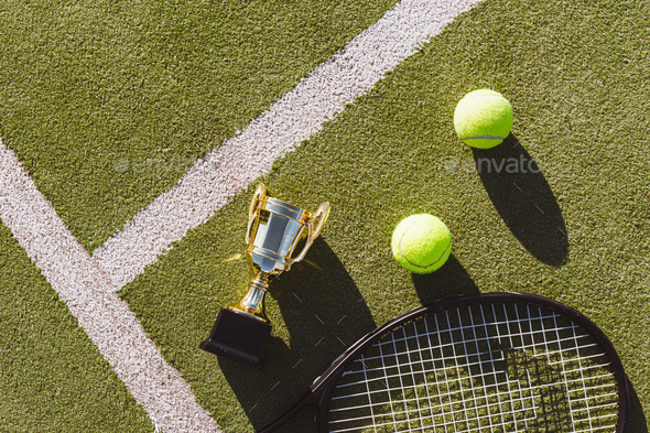 Golden champion cup with tennis racket and balls on playing court.