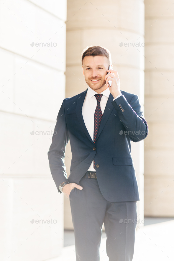 Vertical shot of handsome successful male financial director solves problems via smart phone