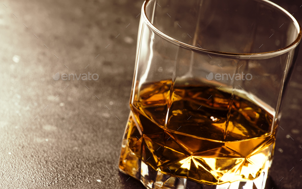 One glass of golden scotch whiskey on dark old bar table background, selective focus